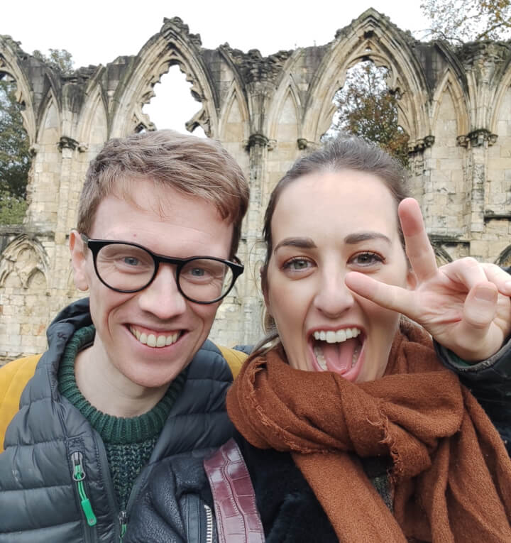 A happy couple smiling at the camera in front of a ruined abbey